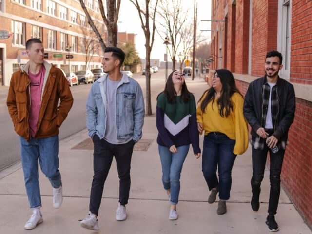 A group of cheerful students walking out of their school building, smiling and talking with each other.