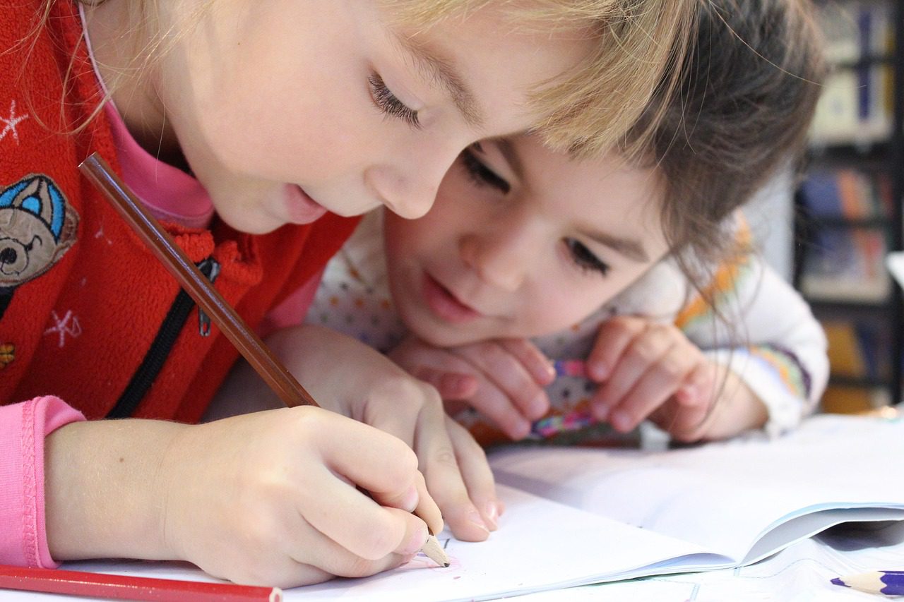 Two young girls engaged in writing together, focusing on improving their handwriting and creative expression.